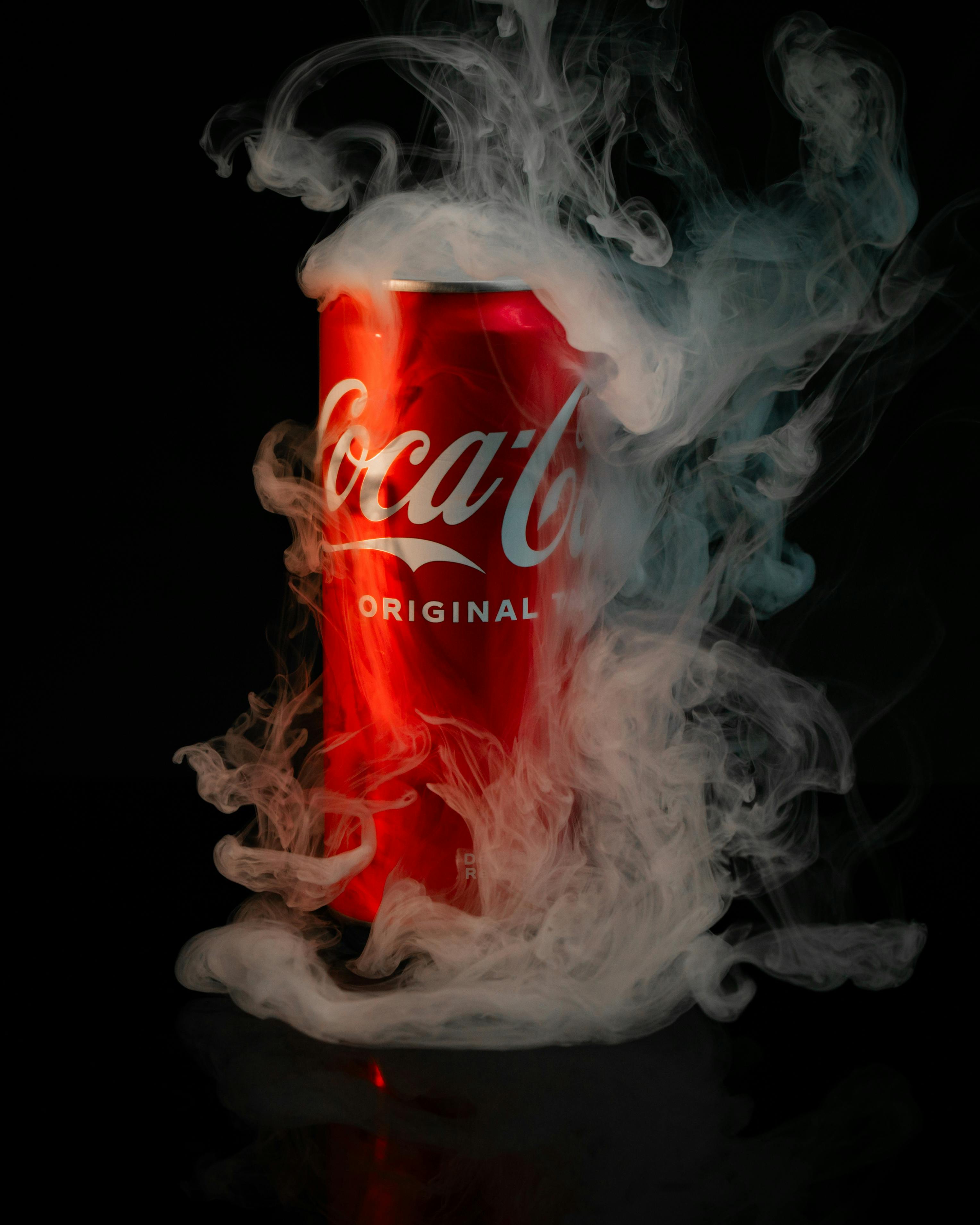 Red Coca-Cola can enveloped in swirling smoke on black background.