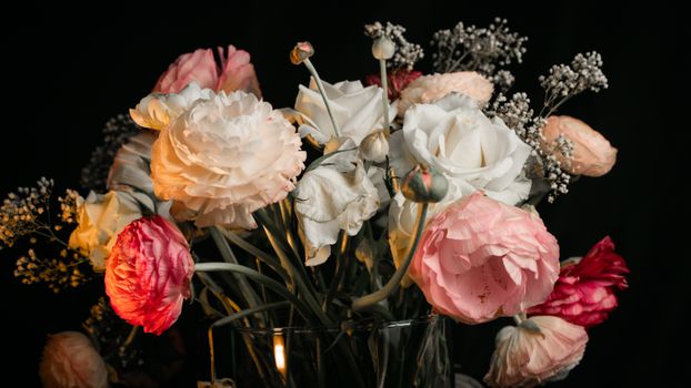 Beautiful arrangement of roses and ranunculus in a vase on a dark background.