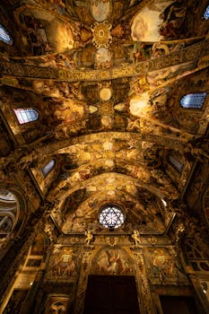 A stunning view of an ornate church ceiling adorned with intricate art and warm lighting.