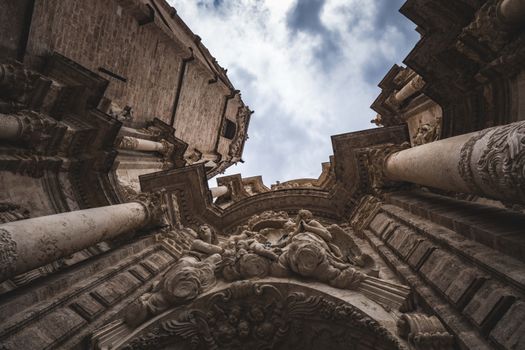 Stunning upward view of an ornate Baroque cathedral facade with dramatic clouds in the sky.