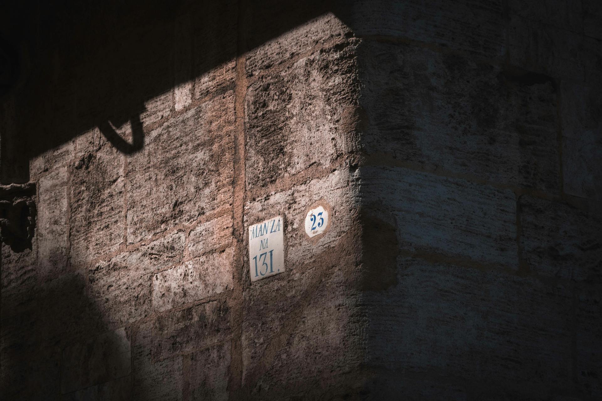 Close-up of an ancient wall corner with street numbers in dramatic lighting.