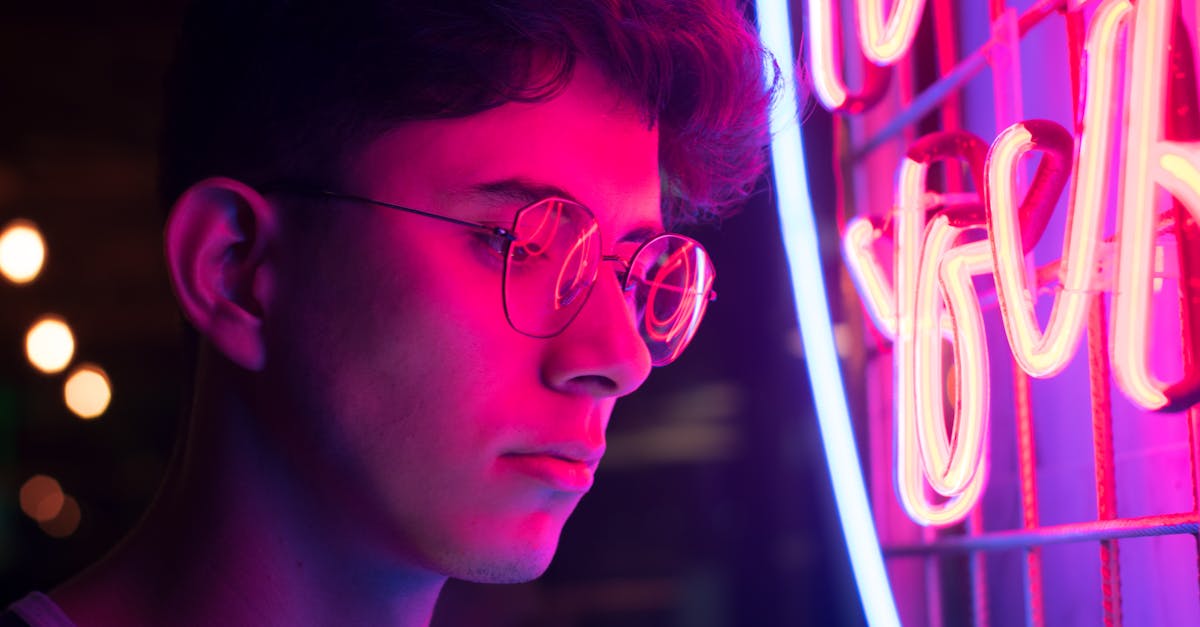 Photo by Viviana Escobar A young man with glasses illuminated by vibrant neon lights in an urban setting.