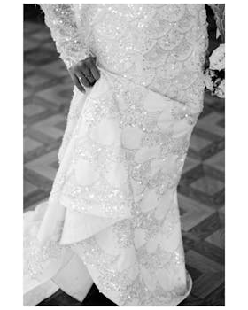 Close-up of a bride holding her sparkling white wedding gown in black and white.