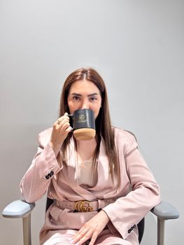 Confident young woman in pink suit sipping coffee during work break.
