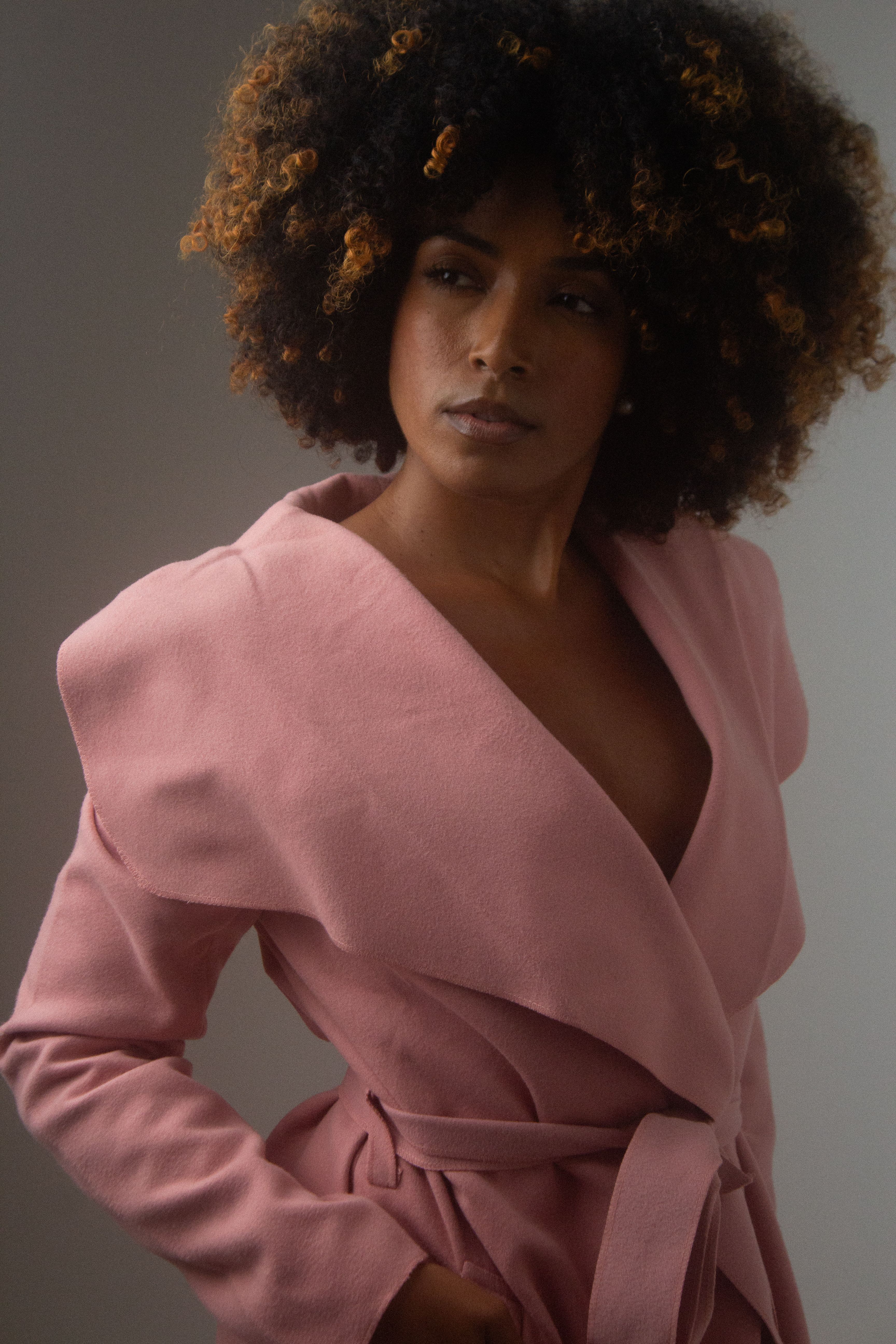 Elegantly posed woman wearing a pink coat, exuding fashion and confidence.