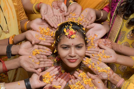 A South Asian bride surrounded by hands with flowers, showcasing traditional wedding customs and henna designs.