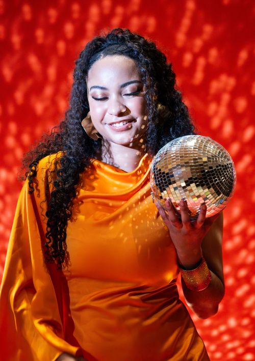Free Portrait of a joyful woman holding a disco ball against a striking red backdrop, creating a festive mood. Stock Photo