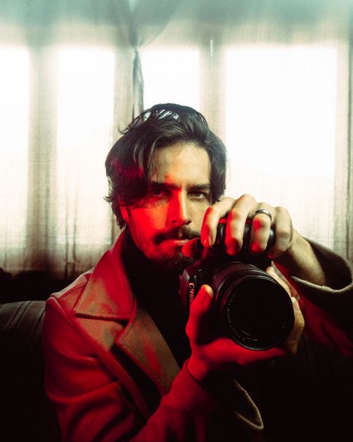 Free Stylish portrait of a male photographer adjusting his camera indoors. Stock Photo