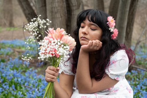 Free A woman in a floral dress holding a bouquet of flowers, surrounded by spring blooms. Stock Photo
