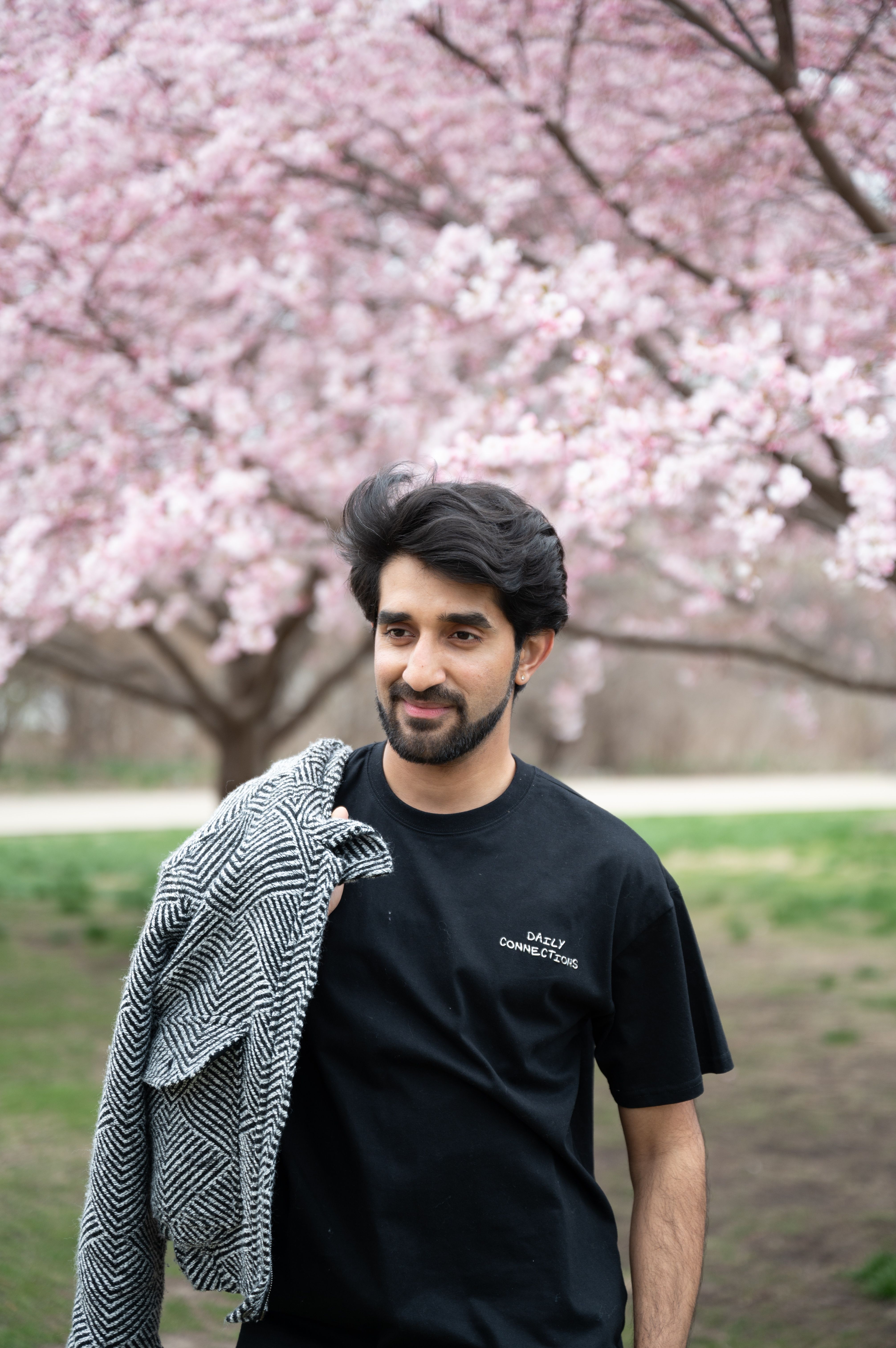 A young man smiling under cherry blossoms in a park during spring, capturing the essence of calm and nature.