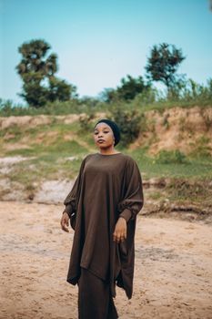 A woman stands gracefully in a brown traditional outfit outdoors, exuding elegance.