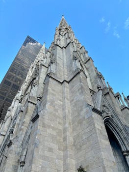 Impressive upward view of St. Patrick's Cathedral showcasing Gothic architecture against a bright blue sky in New York City.