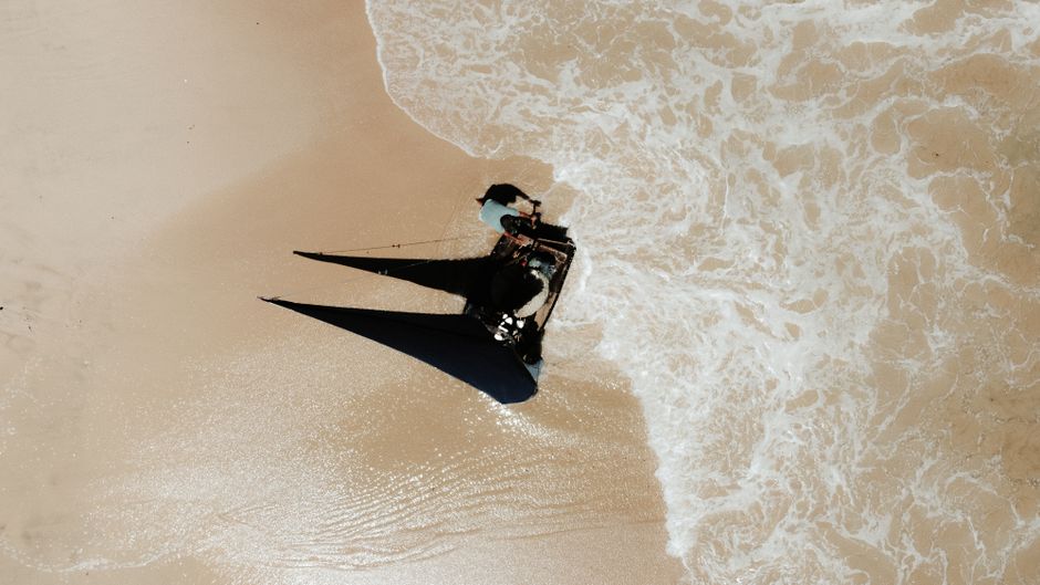 Aerial shot of a boat on a sandy beach in Ceará, Brazil, merging with ocean waves.