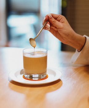 A hand stirs a creamy latte in a cozy cafe setting, creating a warm ambiance.