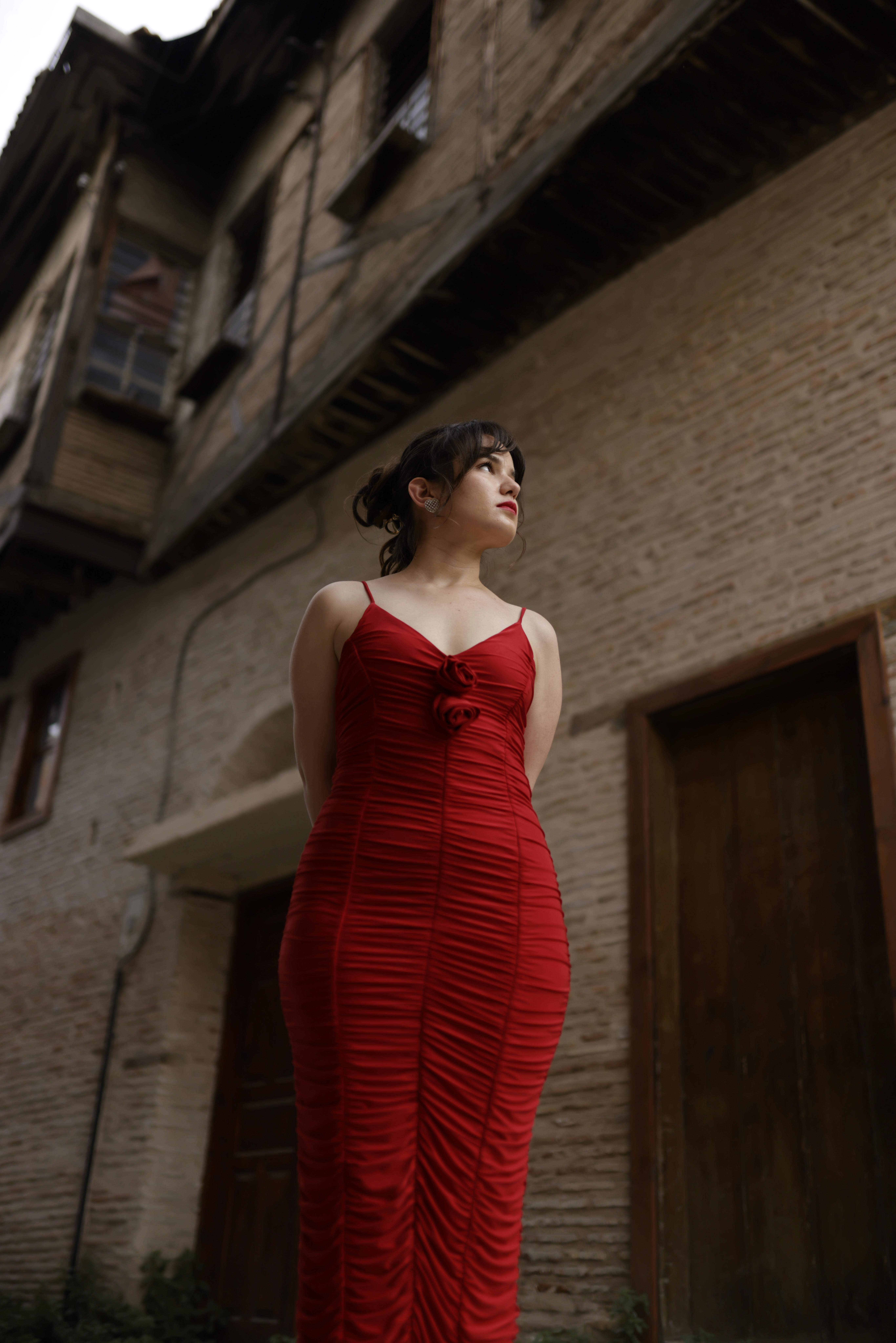 Woman in a striking red dress in front of an old building, showcasing elegance and contrast.