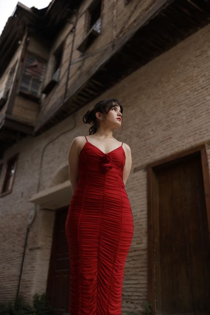 Woman in a striking red dress in front of an old building, showcasing elegance and contrast.