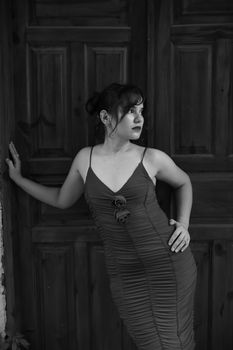 Black and white portrait of a woman in an elegant dress against wooden doors.
