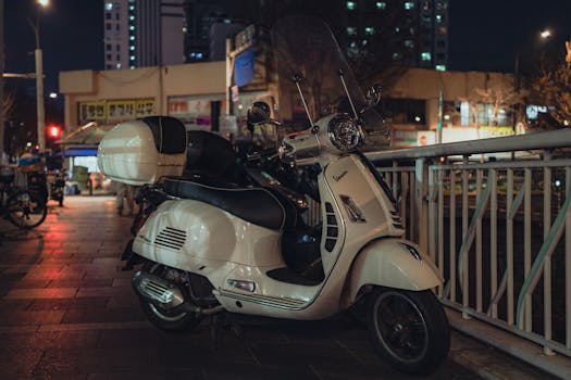 A classic white scooter parked in downtown Seoul at night, highlighting city life.