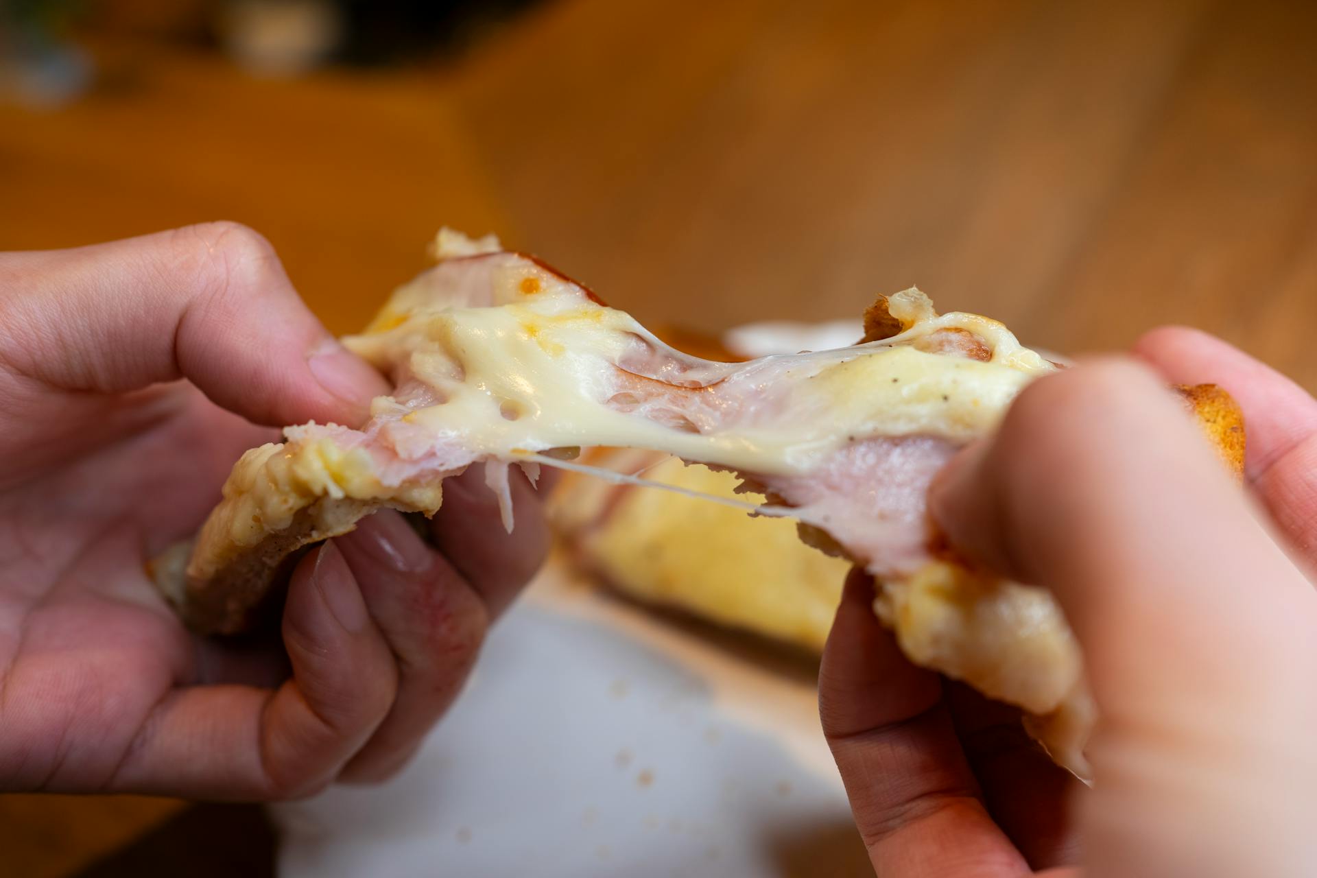 Melted cheese stretching from a hot grilled cheese sandwich being pulled apart, showcasing its gooey texture.