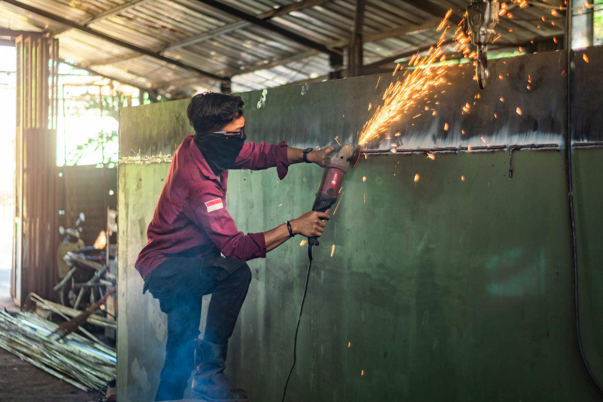 A worker in a workshop using a grinder on metal, emitting bright sparks in an industrial setting.