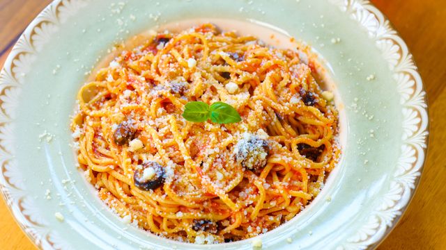 Close-up of a flavorful spaghetti dish topped with olives and parmesan cheese.