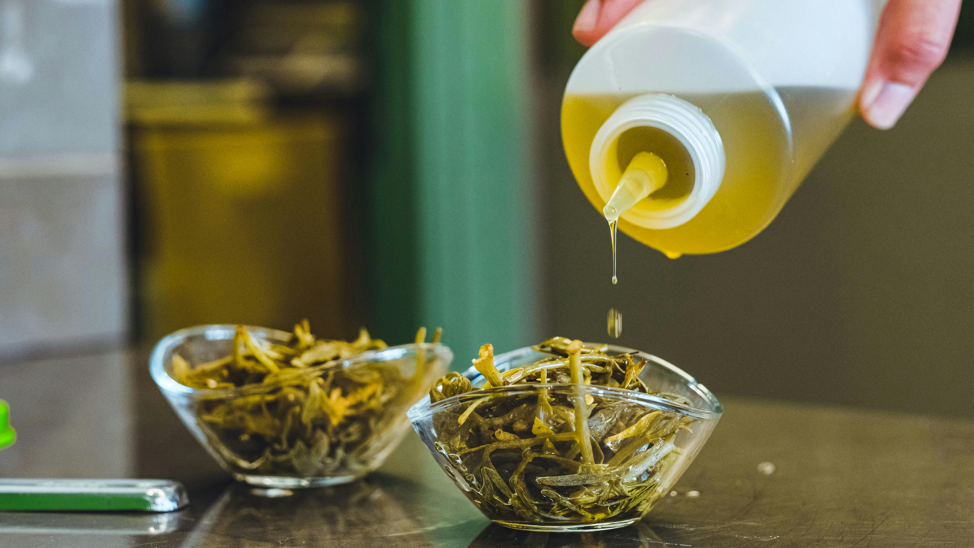 Pouring olive oil over fresh herbs in glass bowls, adding flavor to the dish.