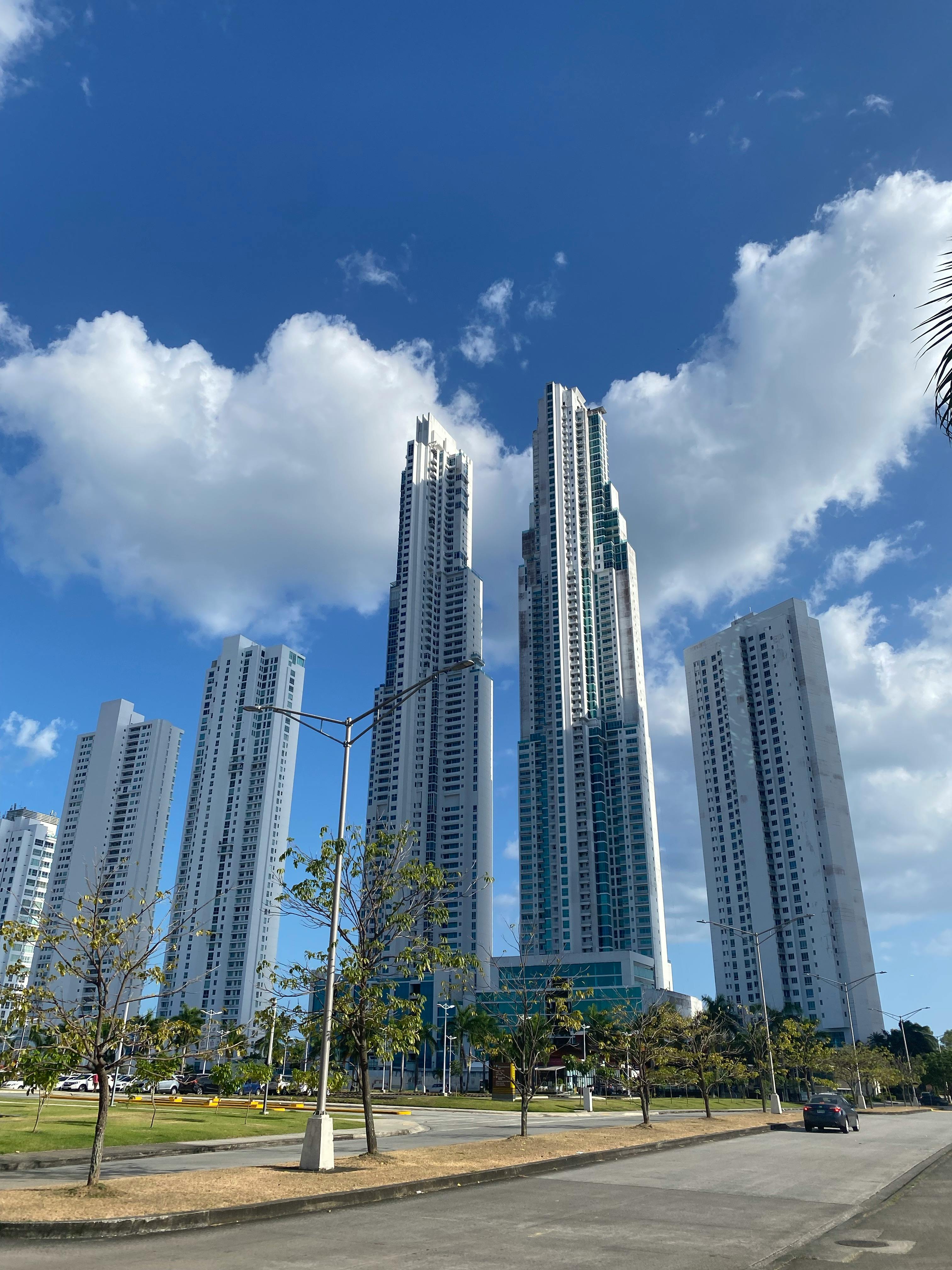 Tall modern skyscrapers soar against a bright blue sky with clouds.