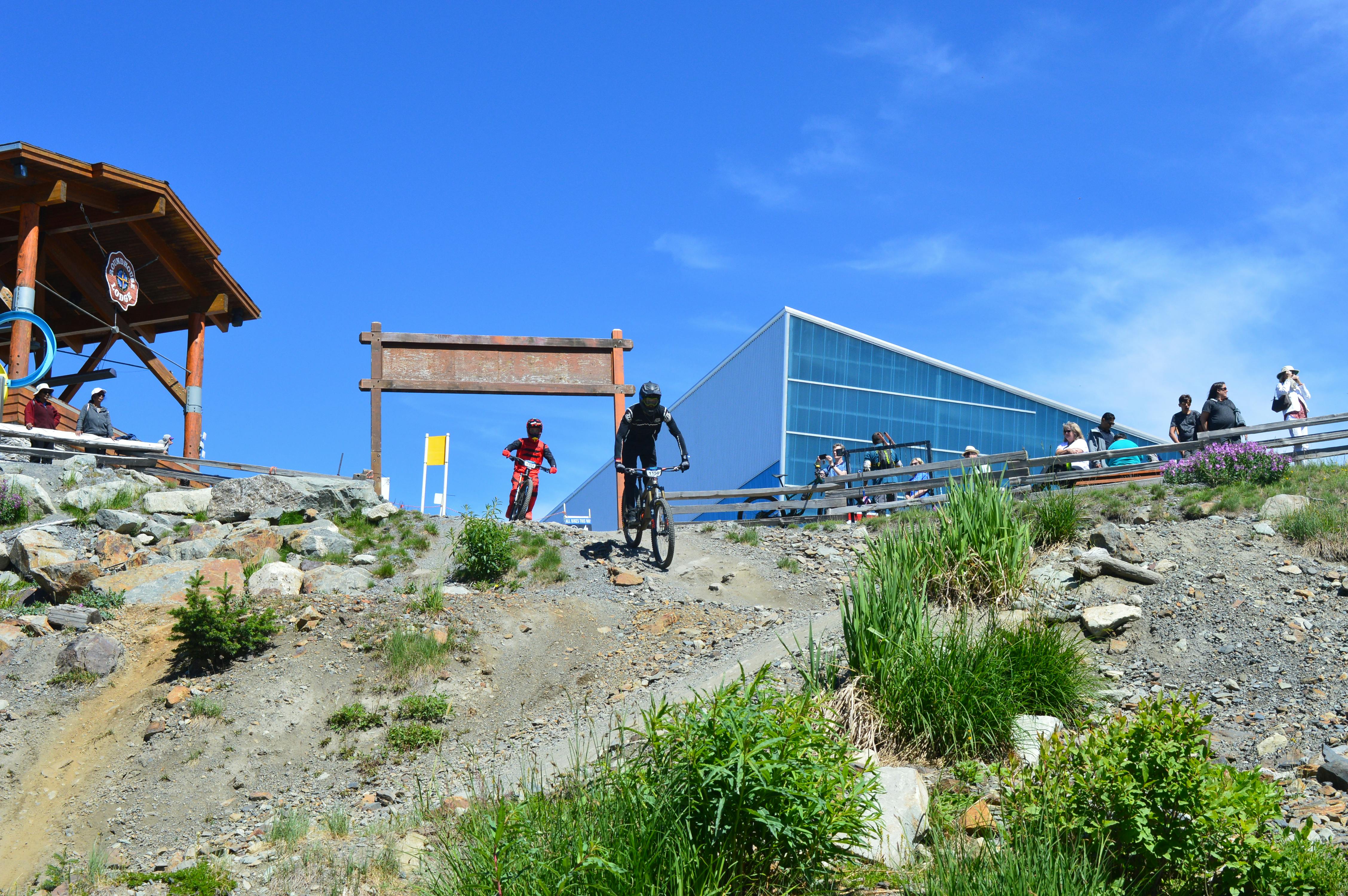 Cyclists descend rocky terrain in Whistler, BC, under clear skies.