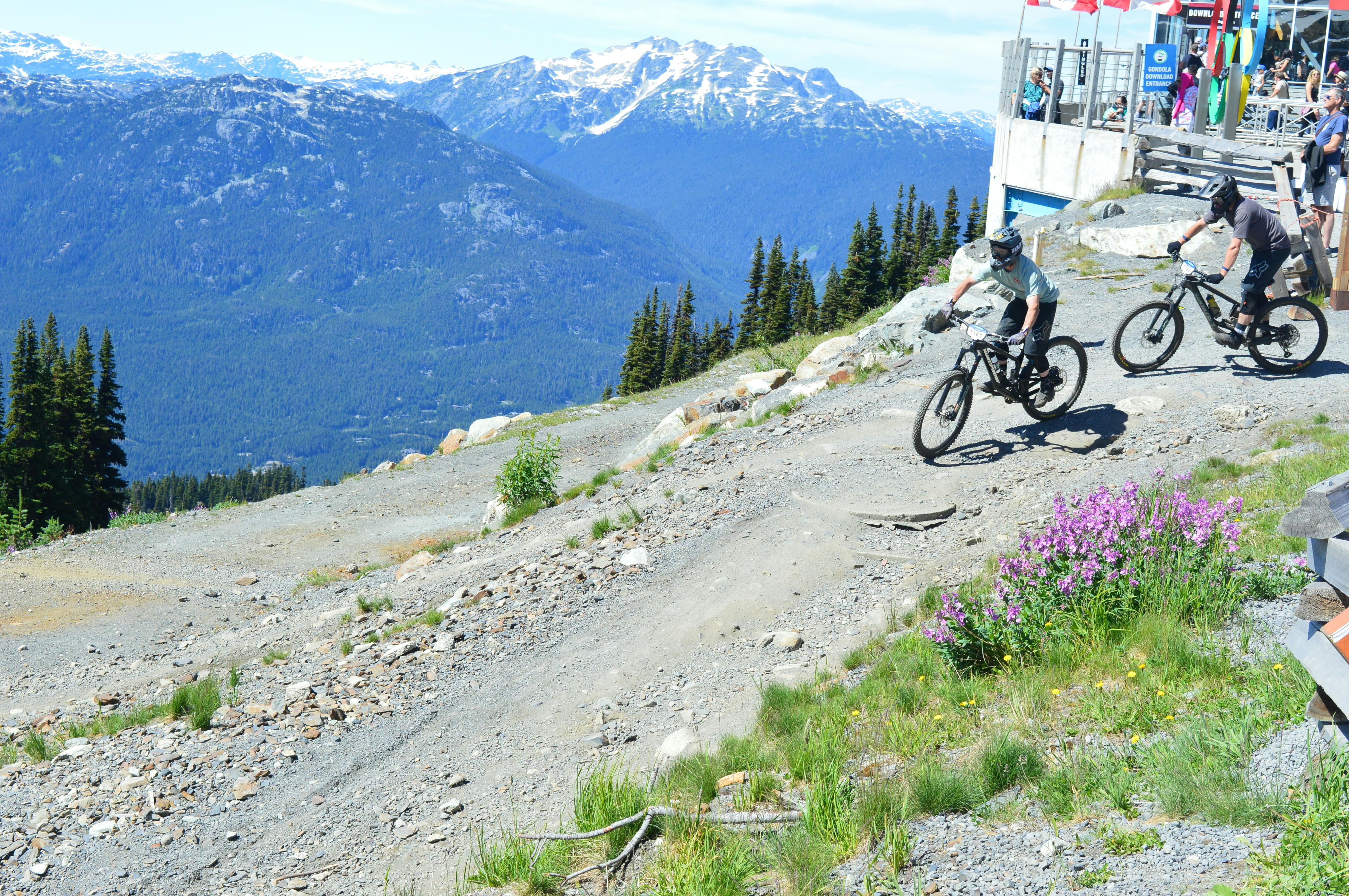 Cyclists racing down a scenic mountain trail in Whistler, BC, with stunning alpine views.