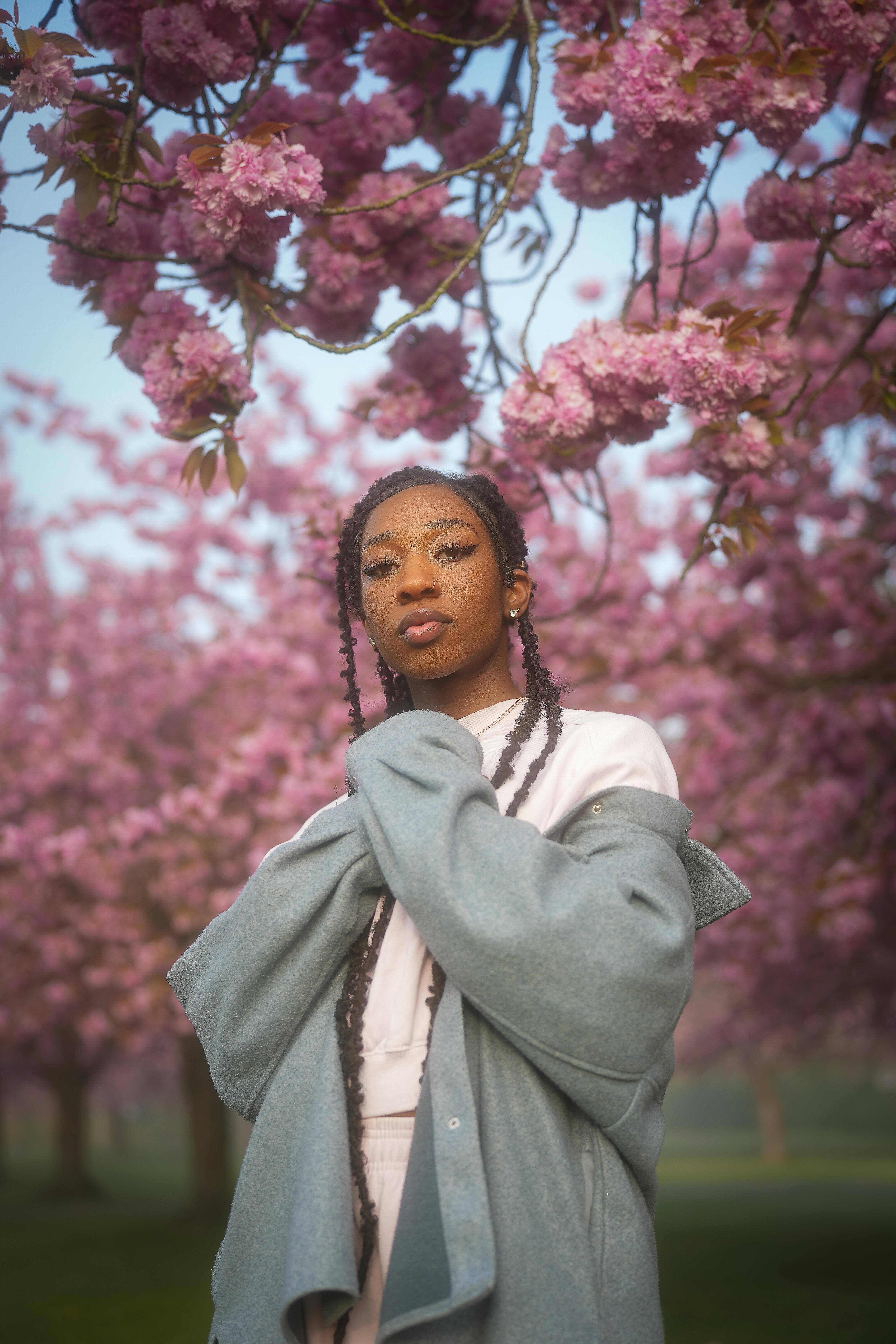 Portrait of a stylish woman surrounded by blooming cherry blossoms in Berlin, showcasing beauty and spring vibrance.