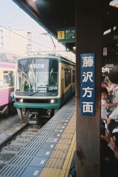 A train arrives at a busy station in Tokyo with people waiting on the platform.