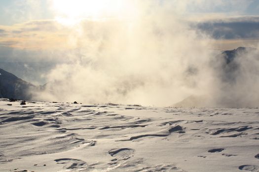 A breathtaking view of snow and clouds on a winter mountain during sunrise.