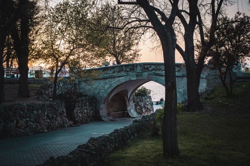 Free A peaceful stone bridge under a tranquil sunset surrounded by lush trees in a park. Stock Photo