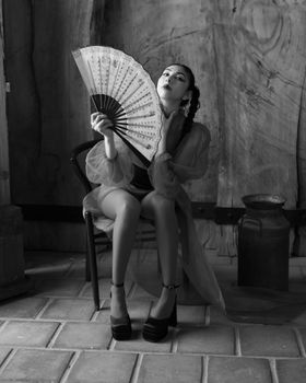 Artistic black and white portrait of a woman with a fan in an indoor setting.