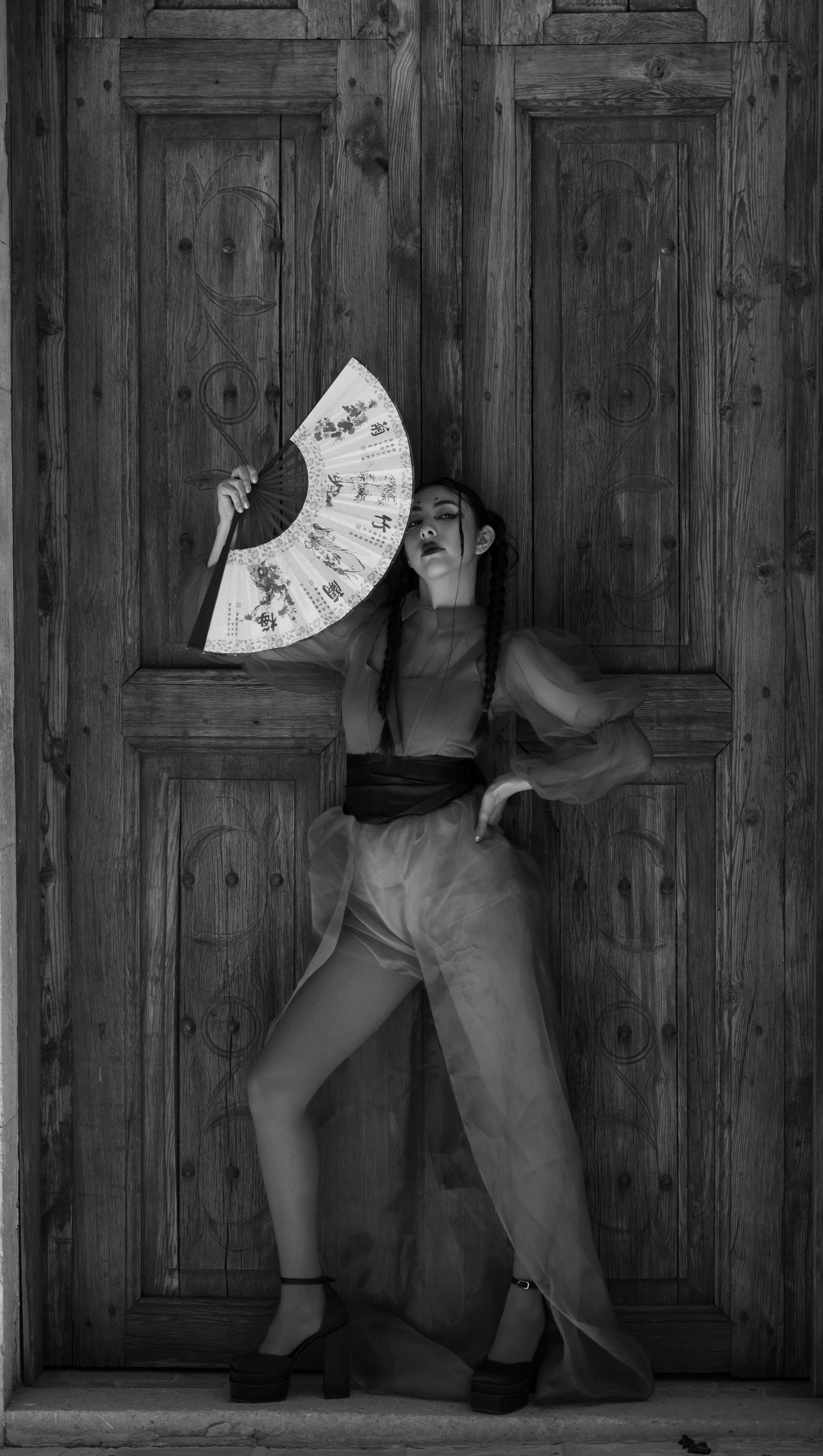 Monochrome portrait of a woman posing with a traditional fan, exuding elegance.