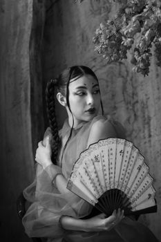 Black and white portrait of an elegant woman holding a fan, depicting traditional Asian fashion with cultural elements.