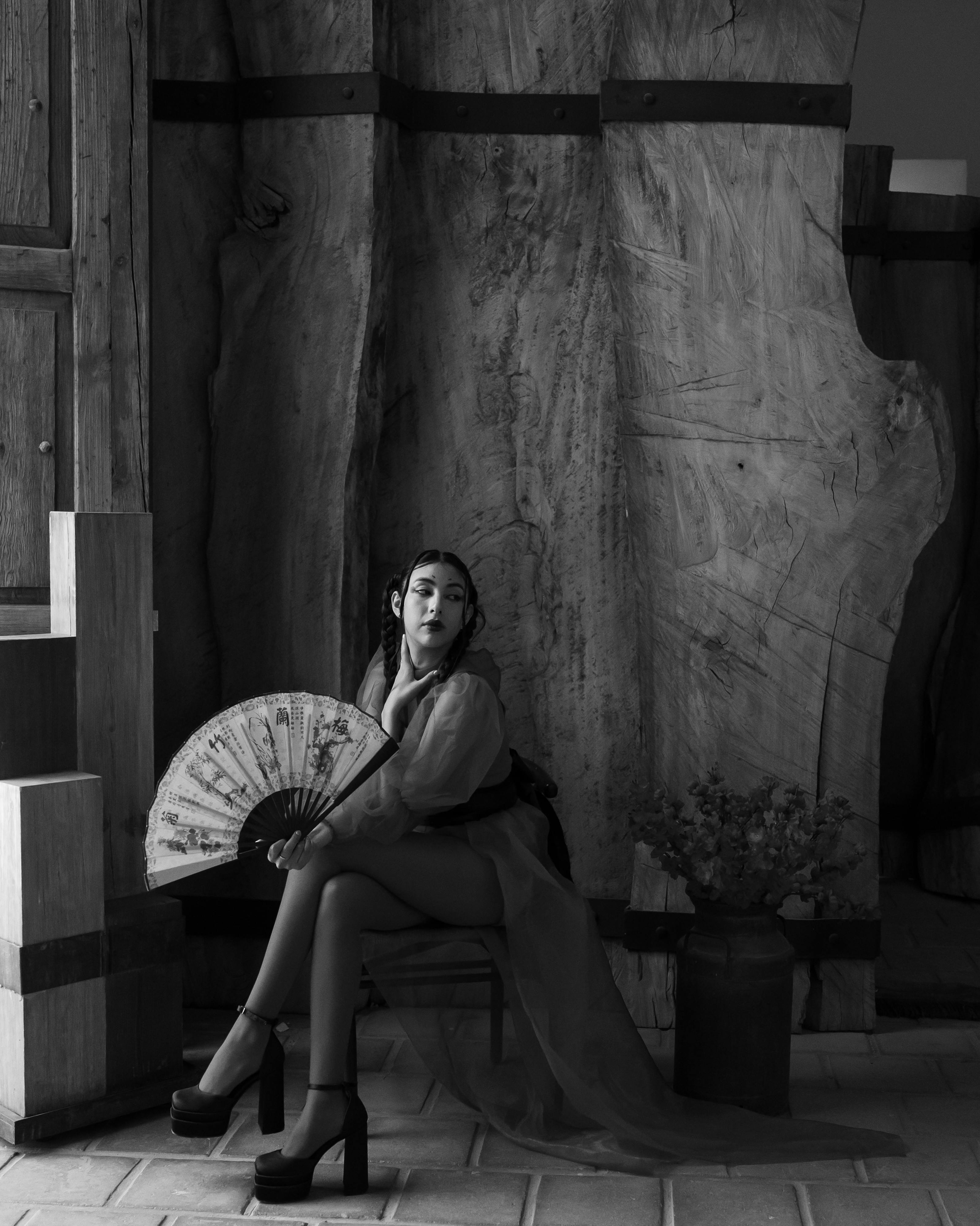 Ücretsiz Kapalı alanda oturan ve elinde dekoratif bir yelpaze tutan bir kişinin çarpıcı siyah beyaz portresi. Stok Fotoğraflar