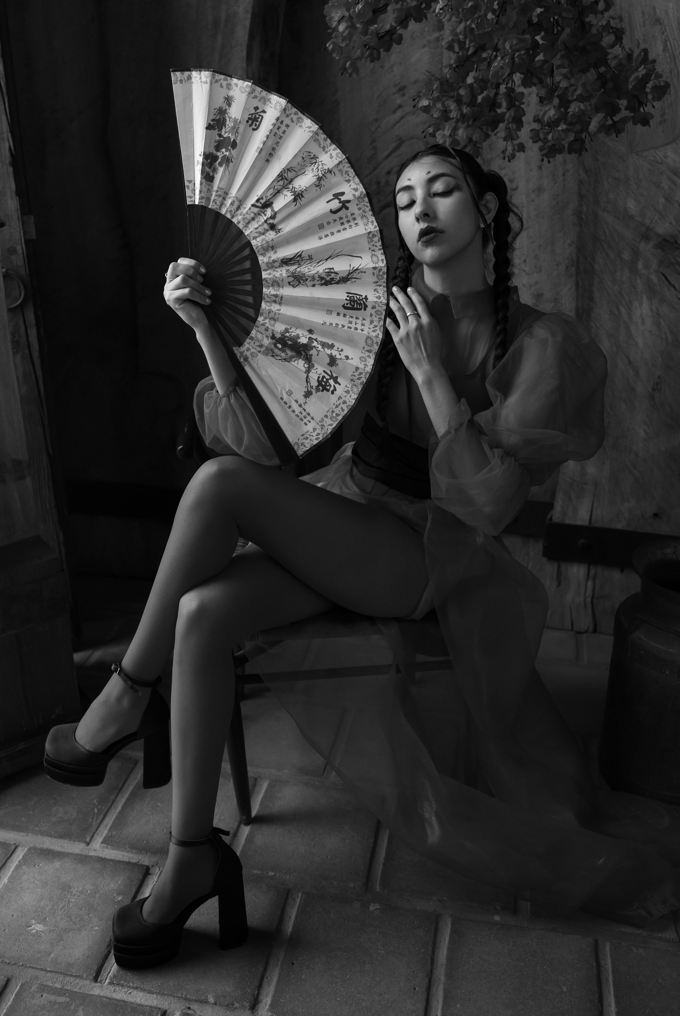 Black and white portrait of a stylish woman seated indoors, holding a decorative fan.