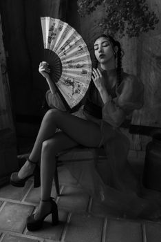 Black and white portrait of a stylish woman seated indoors, holding a decorative fan.