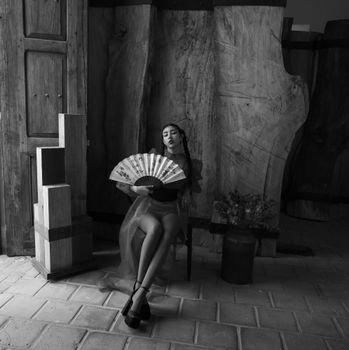 Elegant black and white portrait of a woman sitting with a fan, showcasing sophisticated artistic styling.