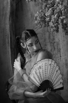 Black and white portrait of a woman holding a traditional hand fan, exuding elegance and grace.