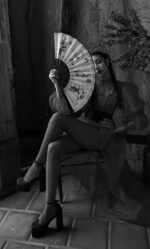 Stylish portrait of a woman holding a fan, seated indoors, in black and white.