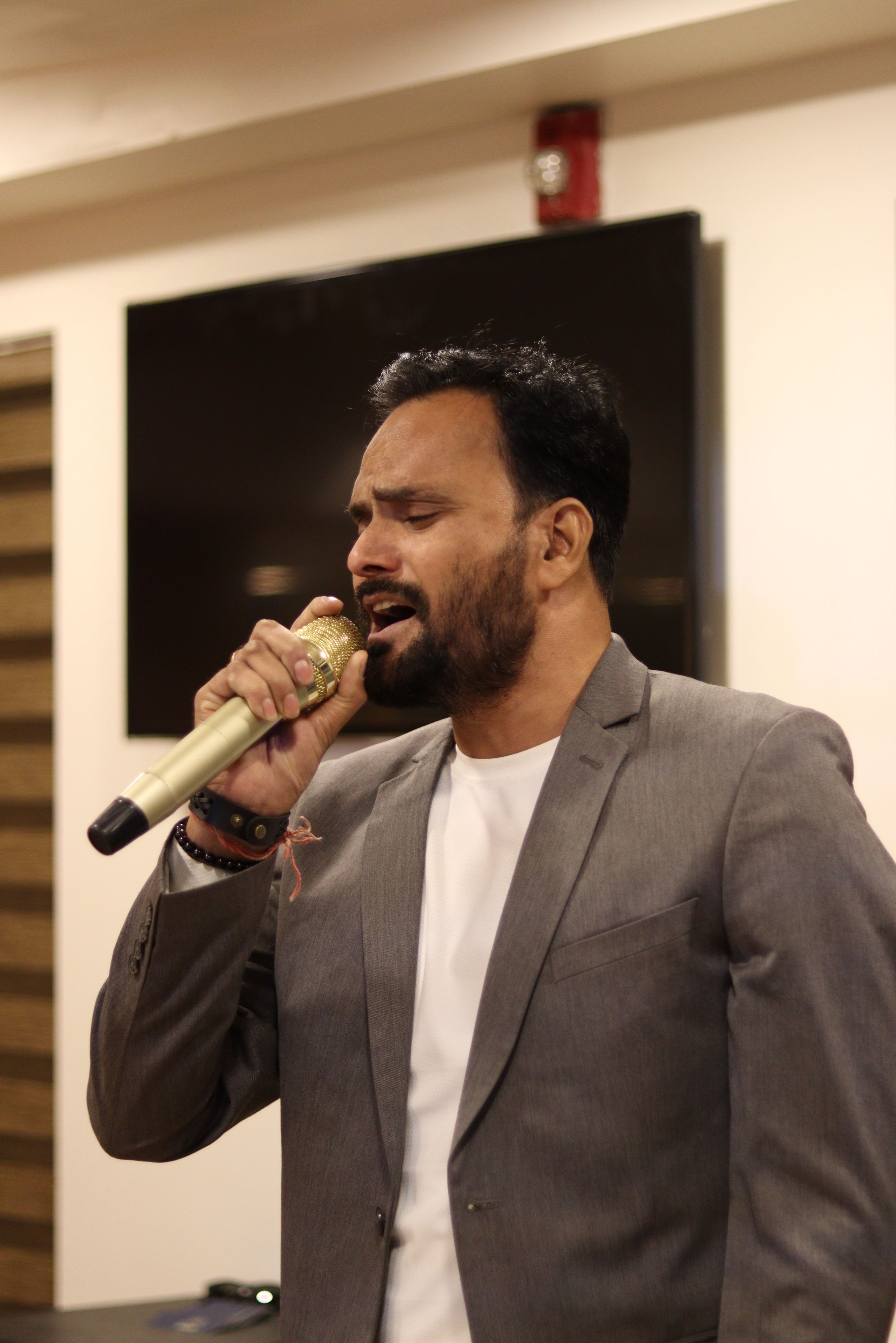 A man in a suit sings passionately into a microphone at an indoor event.
