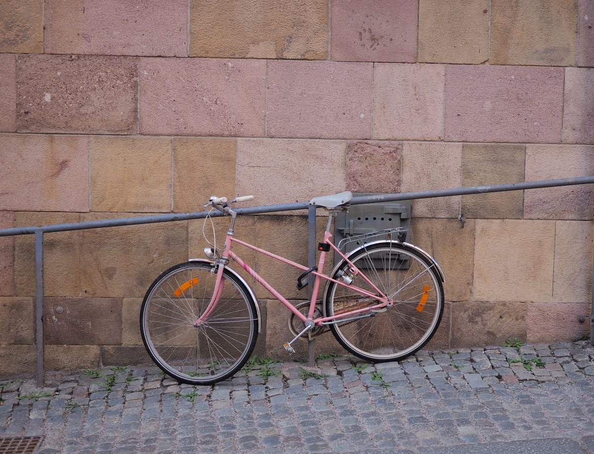 Bicicleta roz pal rezemata de un zid de piatra pe o strada pavata