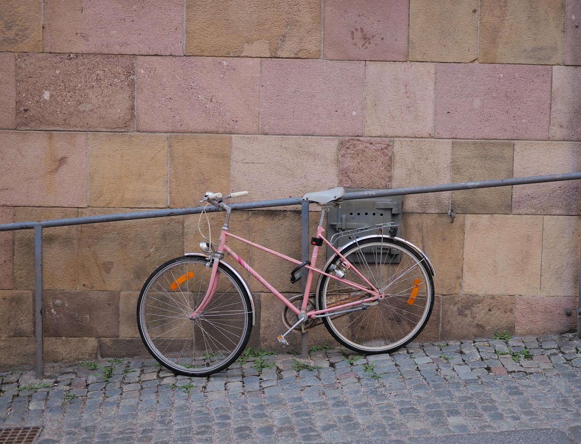 A pale pink bicycle leans against a stone wall on a cobbled street in Stockholm, Sweden.