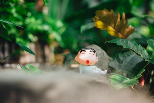 Toy figure resembling a cartoon character among vibrant green plants creating a playful outdoor scene.