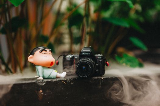 Charming scene with a playful figurine next to a vintage camera amidst a misty, lush backdrop.
