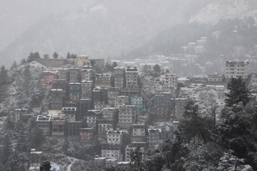 Scenic winter view of snow-covered buildings nestled in Shimla's hills, Himachal Pradesh, India.