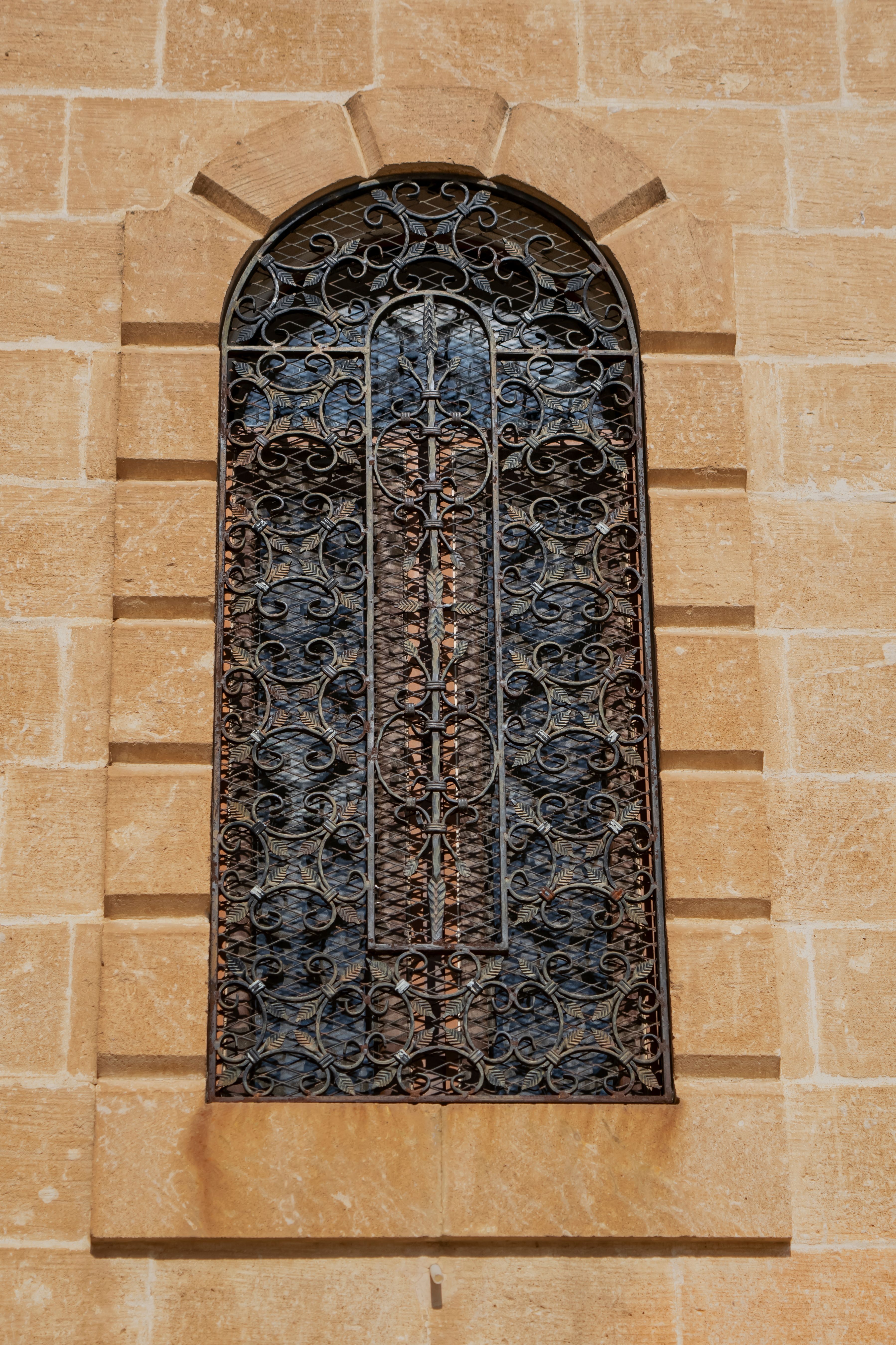 An elegant ironwork window set in a historic stone building facade, showcasing intricate metal designs.