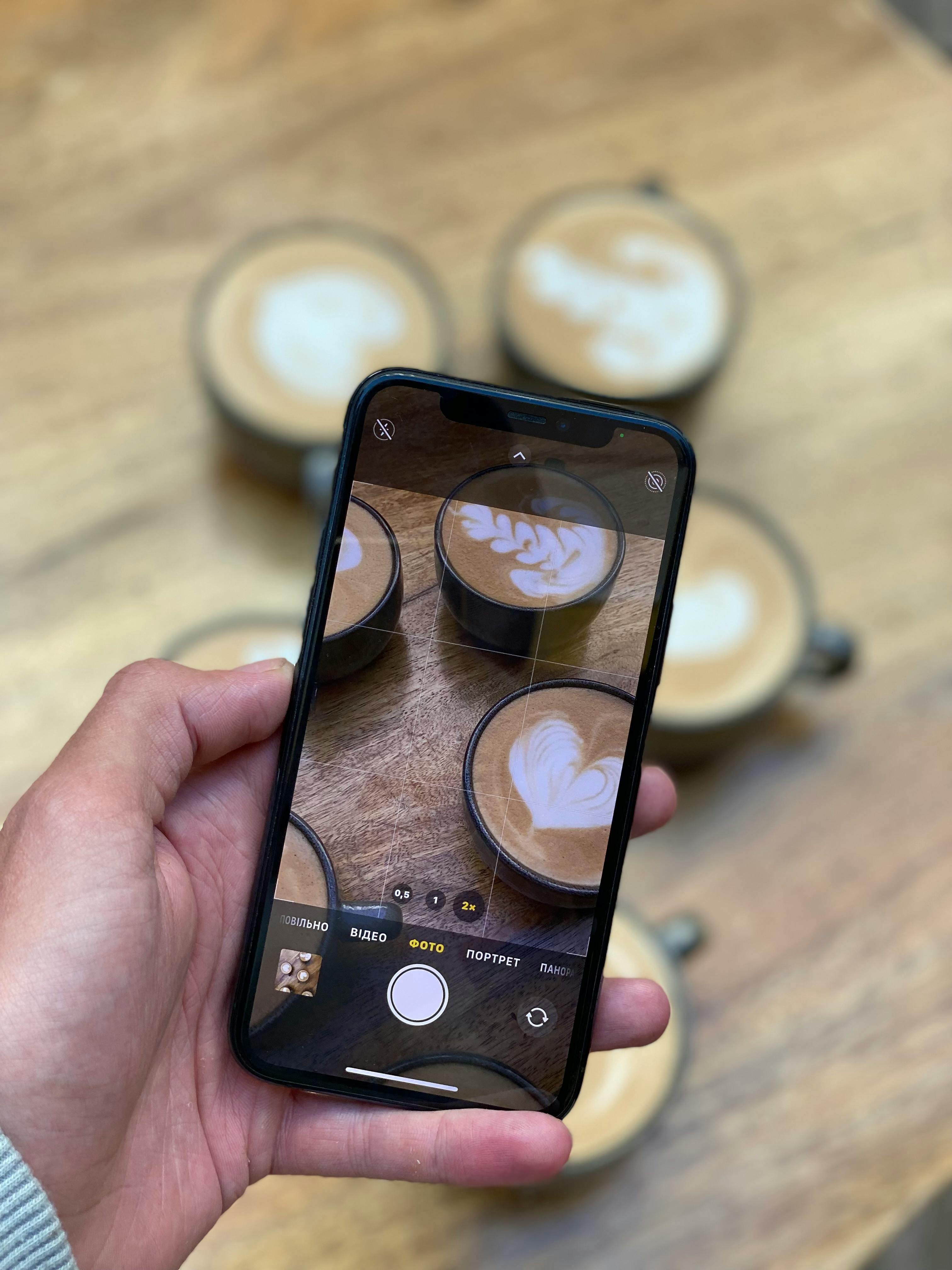 Free Capturing latte art in cups through a smartphone camera, perfect for coffee enthusiasts. Stock Photo